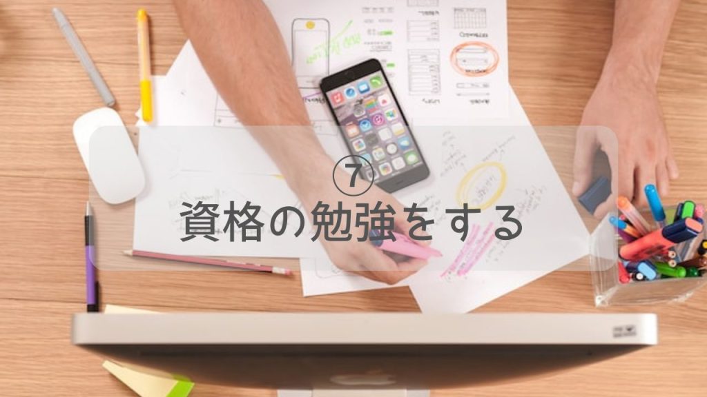 机に広げられたペンや紙とスマホとピンクのペンを持った男性の手