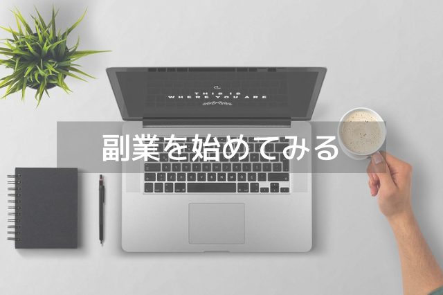 机の上に置かれたMacのパソコンとコーヒーが入ったカップを持つ男性の手